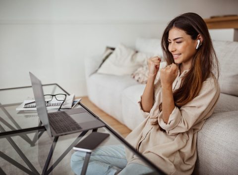 Alegre millennial mestiza con gafas y auriculares inalámbricos tiene videollamada en el ordenador portátil