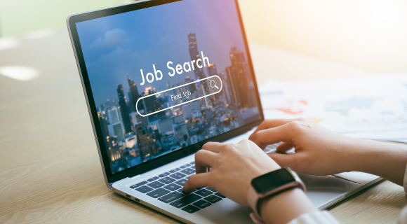 Person typing on a laptop with a “Job Search” screen displayed, showing a cityscape background.