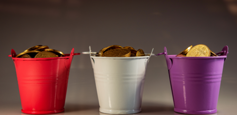 Metal buckets in red, white, and purple, each overflowing with gold coins against a neutral background.