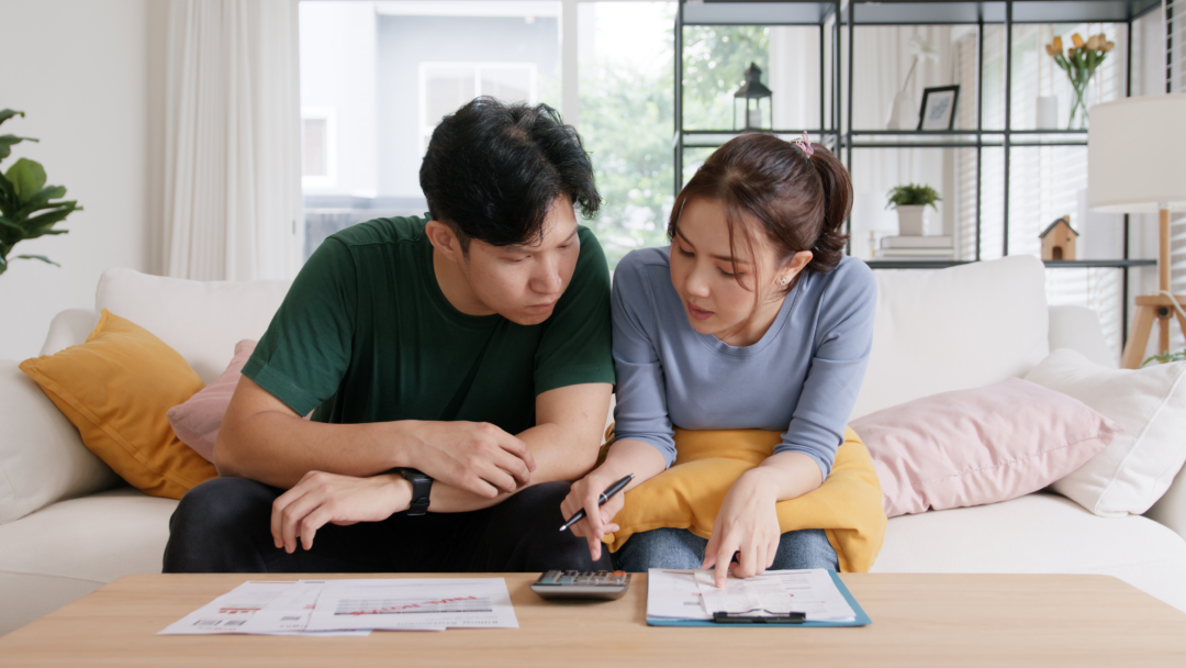 Young partners budgeting together on the couch with paperwork and a clipboard.