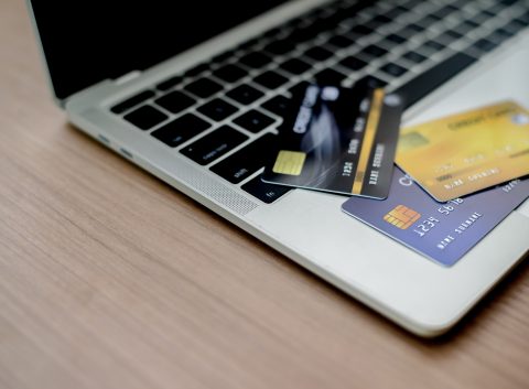 Several credit cards spread across a laptop keyboard on a wooden desk