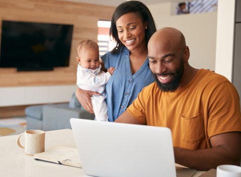 A smiling couple with their baby looking at a laptop together in a modern living room.