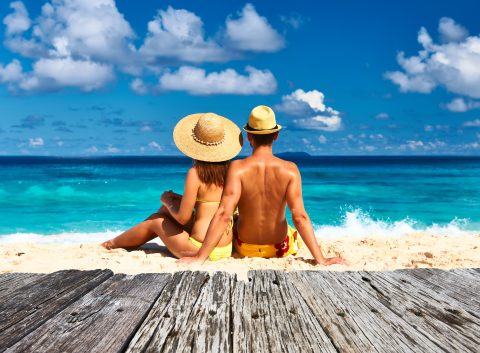 A couple on their honeymoon sitting on a tropical beach in their swimsuits.