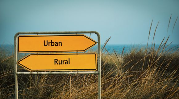 A directional sign by a lake points two ways — left for “rural,” and right for “urban.”