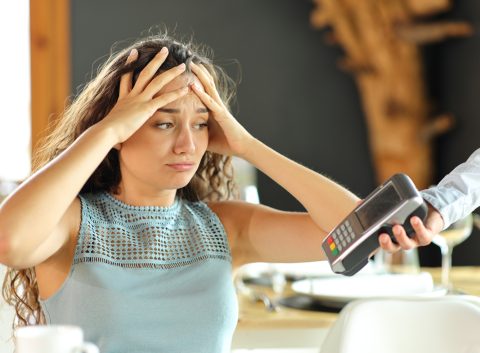Una persona preocupada se echa las manos a la cabeza cuando el camarero de un restaurante extiende hacia ella un terminal de pago para abonar la cuenta.