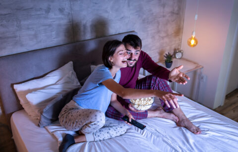 Couple watching a movie and eating popcorn in bed