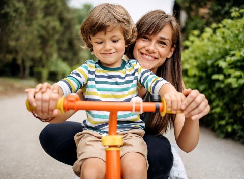 mamá y niño sonriendo y de pie detrás de la bicicleta