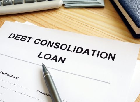 Debt consolidation loan application form with pen on a wooden desk, next to a calculator, money, and notebook.