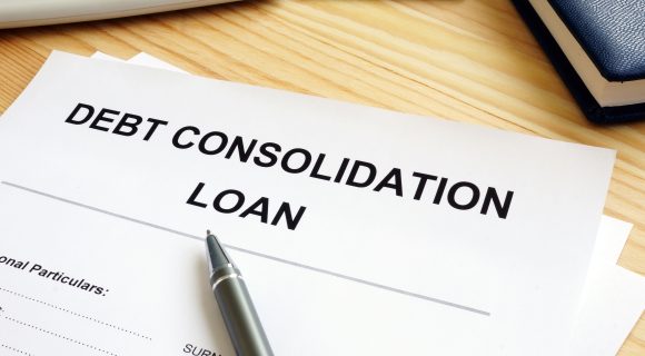 Debt consolidation loan application form with pen on a wooden desk, next to a calculator, money, and notebook.