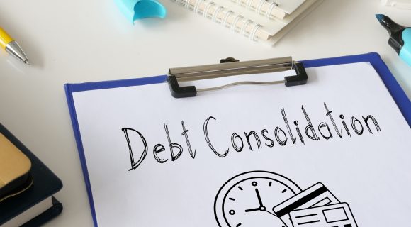 Clipboard with paper labeled “Debt Consolidation” and illustrations of a clock and credit cards, surrounded by office supplies.