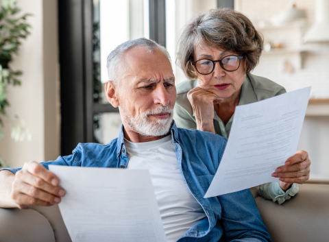 Concerned senior couple sitting on a couch reviewing financial documents together.