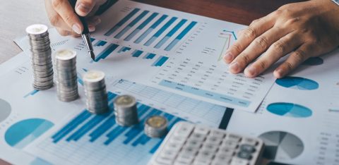 Close-up of a person analyzing financial charts with stacked coins and a calculator on the desk.