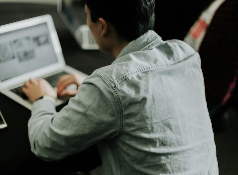 Rear view of a person typing on a laptop at a dark table, with a smartphone placed nearby