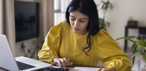 Woman in yellow shirt looking at calculator and paper