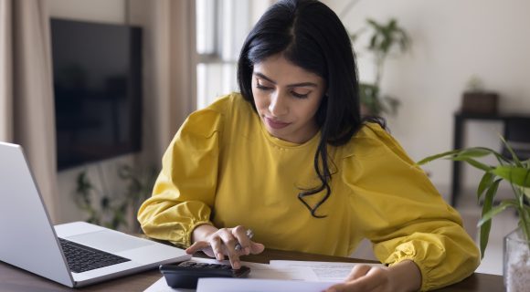 Woman in yellow shirt looking at calculator and paper