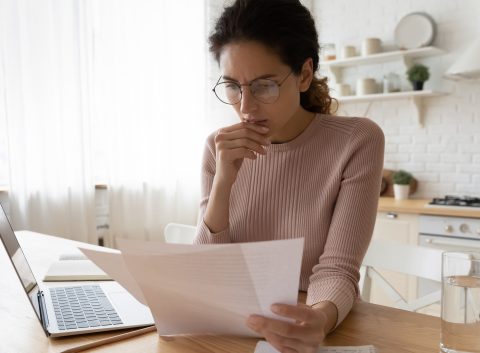 woman looking at computer and paper bills