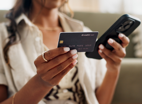 Woman holding a credit card in one hand and a smartphone in the other, possibly making an online purchase.