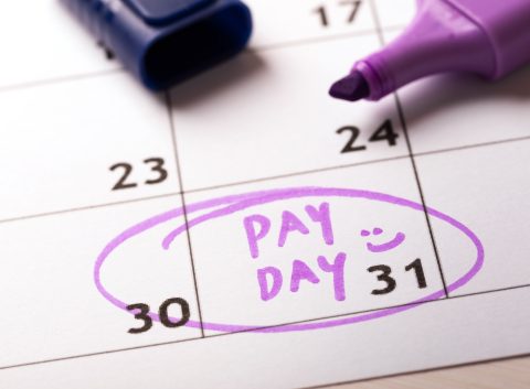 Close-up of a calendar with "PAY DAY" written in purple marker on the 31st, circled with a smiley face, alongside an open marker.