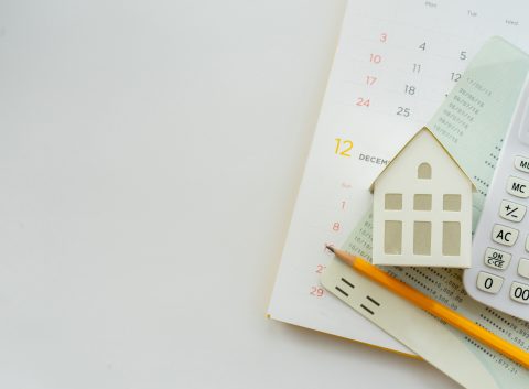 Un calendario, un modelo de casa en miniatura, una calculadora y documentos financieros dispuestos sobre un escritorio, simbolizando la planificación de una hipoteca y la propiedad de una vivienda.