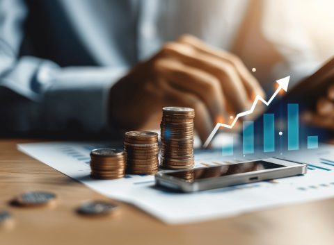 Stacks of coins on financial documents with a smartphone and a digital growth chart overlay