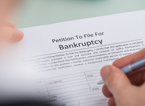 Close-up of a person filling out a petition to file for bankruptcy form with a pen.
