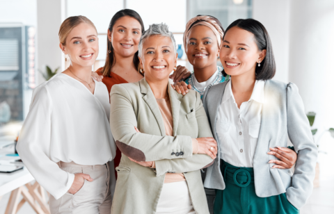 A diverse group of confident professional women smiling together in a modern office setting.