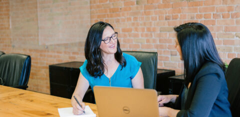 Two professional women having a friendly conversation during a meeting in a modern office.