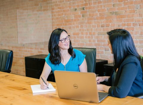 Two professional women having a friendly conversation during a meeting in a modern office.