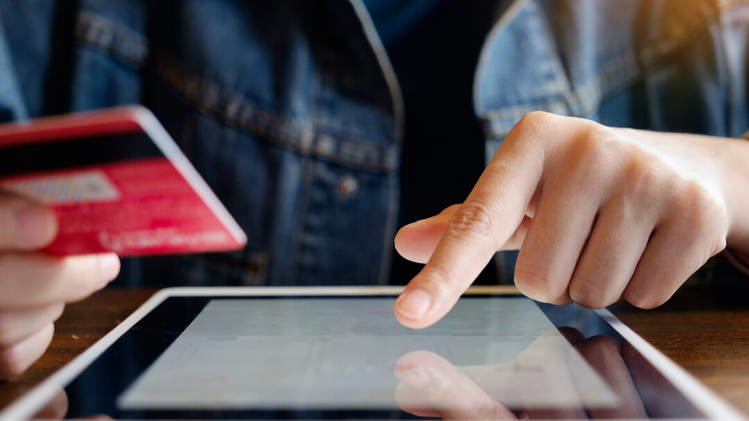 person holding credit card and typing on tablet
