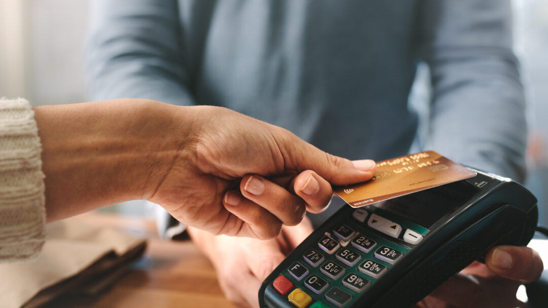 A person making a contactless payment with a credit card at a point-of-sale terminal.