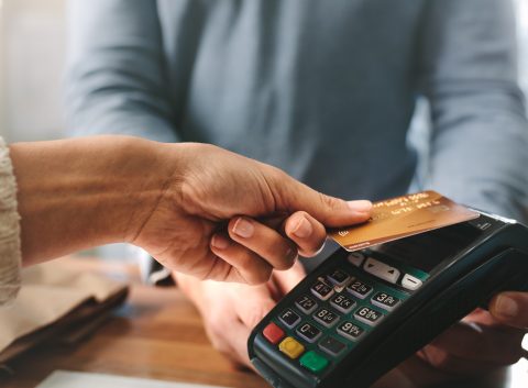 A person making a contactless payment with a credit card at a point-of-sale terminal.