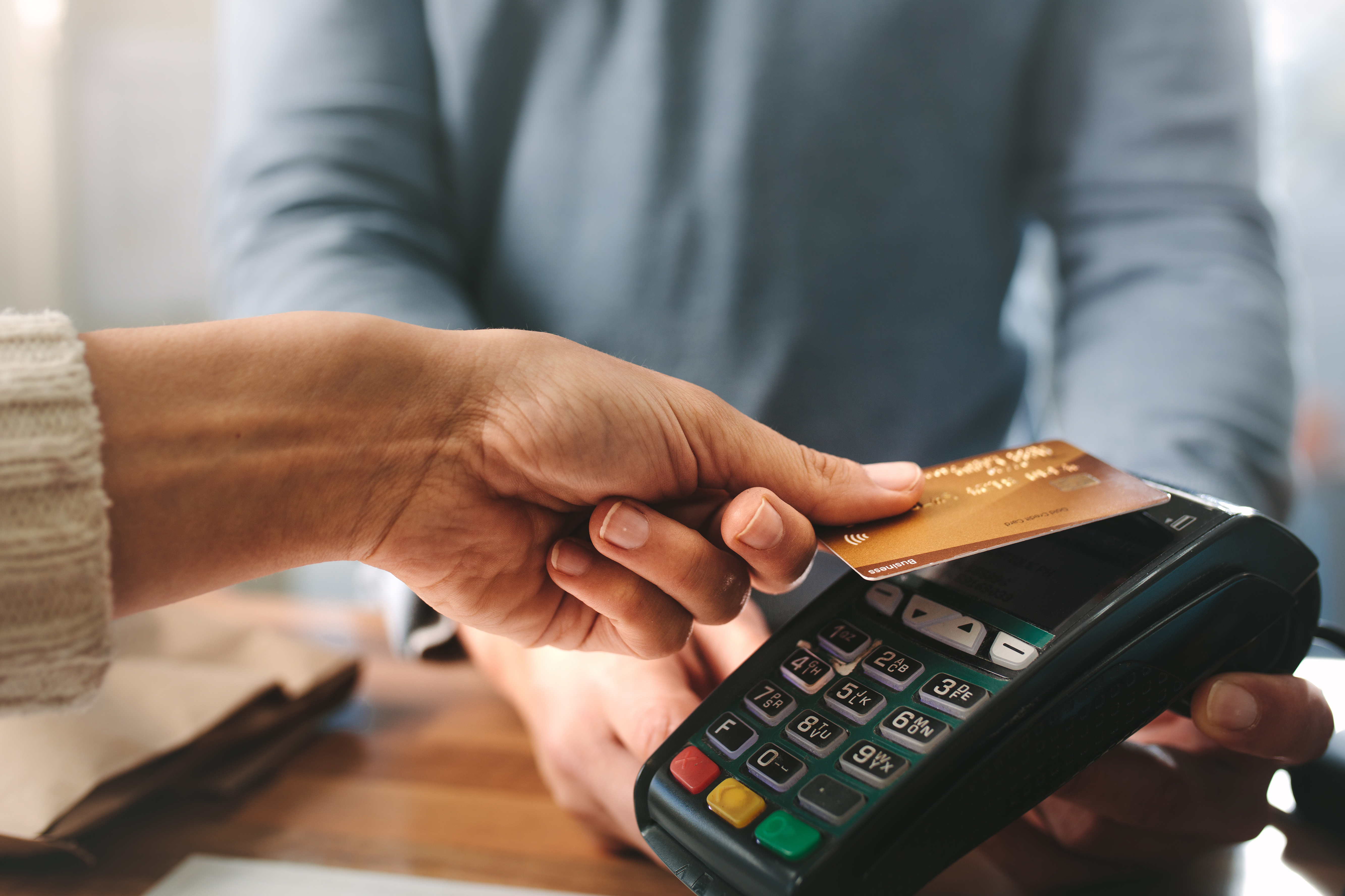 A person making a contactless payment with a credit card at a point-of-sale terminal.