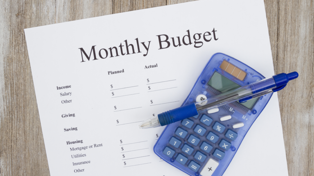 Monthly budget worksheet with a pen and calculator on a wooden table.