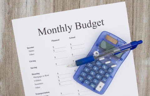 Monthly budget worksheet with a pen and calculator on a wooden table.
