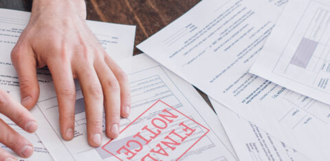 A person's hand resting on a stack of financial documents, with one paper prominently stamped “FINAL NOTICE” in red.