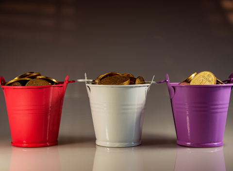Three colorful buckets—red, white, and purple—filled with gold coins, symbolizing savings categories or budgeting strategies.