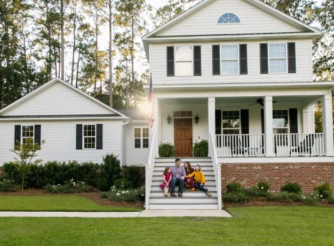 Family sitting on the front steps of a white suburban home with black shutters, enjoying time together outdoors.