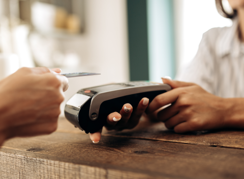 Close-up of a credit card being tapped on a card reader, with a cashier holding the payment terminal.
