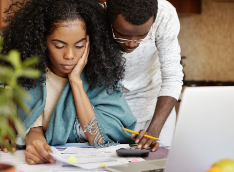 Couple reviewing financial documents together at home, looking concerned.