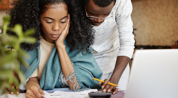 Couple reviewing financial documents together at home, looking concerned.