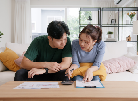 Young couple sitting on a couch, focused on calculating finances with bills and documents spread out on the table.