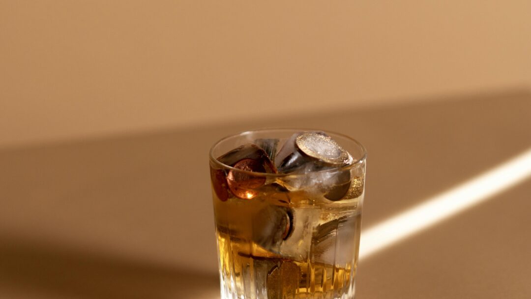 Glass of whiskey on a tan surface with coins and ice cubes inside