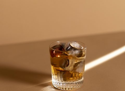Vaso de whisky sobre una superficie bronceada con monedas y cubitos de hielo en su interior