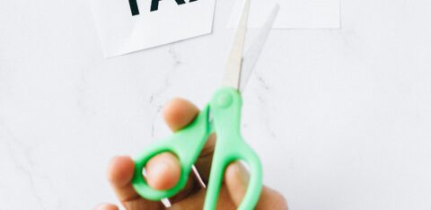 Close-up of a person cutting a “TAXES” sign with scissors