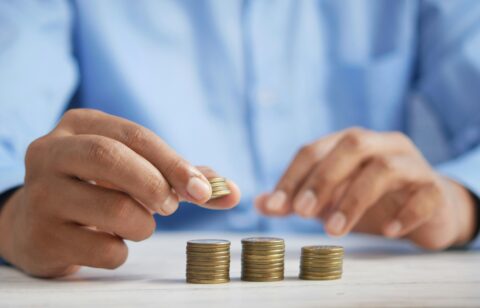 Person in a blue shirt stacking coins into neat piles on a white table, symbolizing budgeting or saving money.