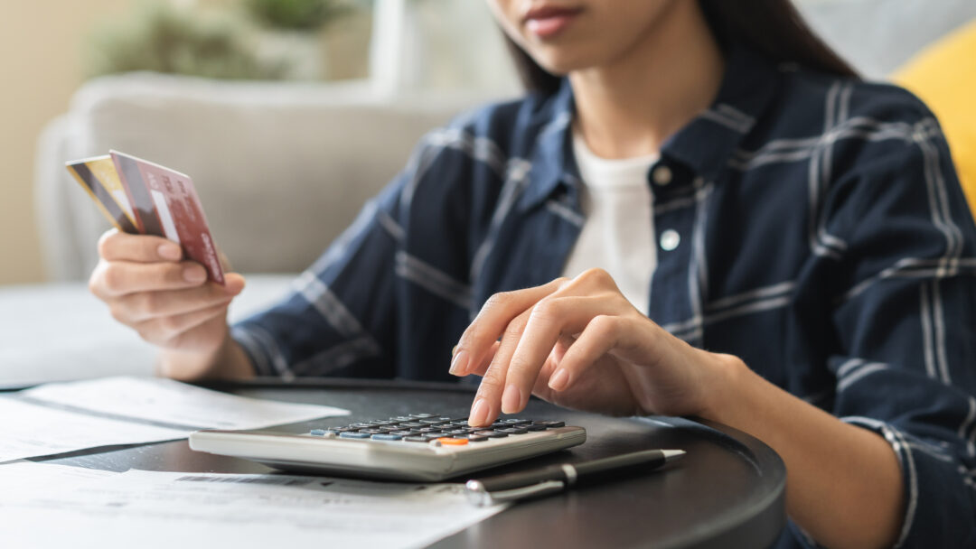 Woman calculating expenses with a credit card in hand, surrounded by bills and financial documents.