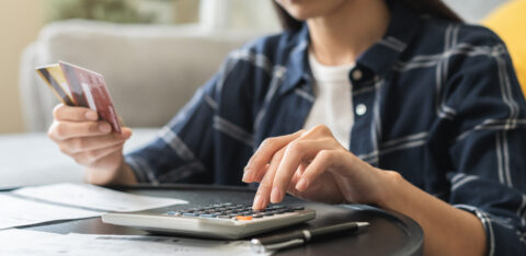 Woman calculating expenses with a credit card in hand, surrounded by bills and financial documents.