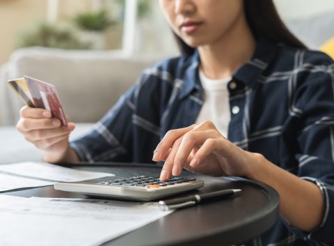 Woman calculating expenses with a credit card in hand, surrounded by bills and financial documents.