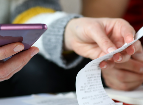 Close-up of two people reviewing a receipt and using a smartphone, suggesting budgeting or expense tracking.