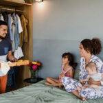 A father brings breakfast in bed to a smiling mother and their two children, celebrating a relaxed morning at home.